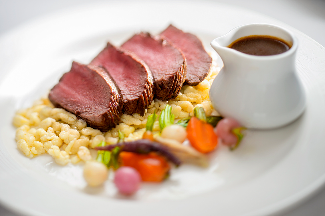 Un carré d'agneau en croûte servi sur des échalotes garnies de romarin