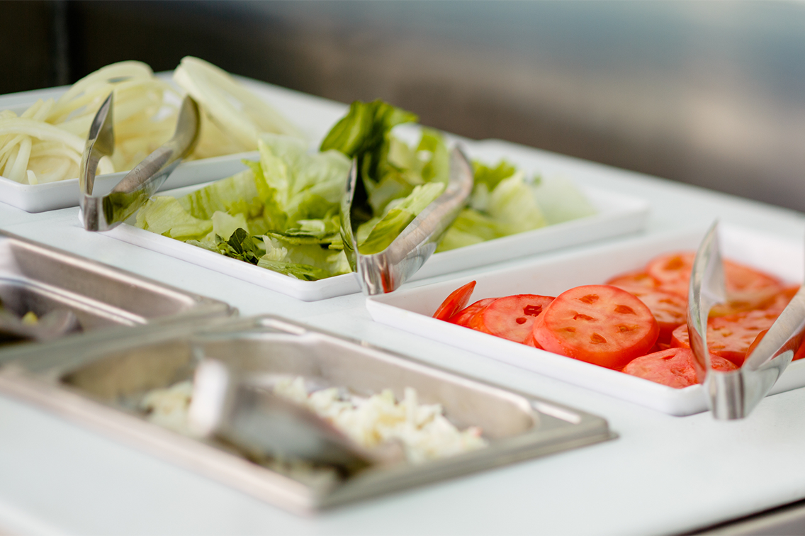 Plusieurs bols carrés remplis de différentes salades, avec des pinces reposant sur chacun