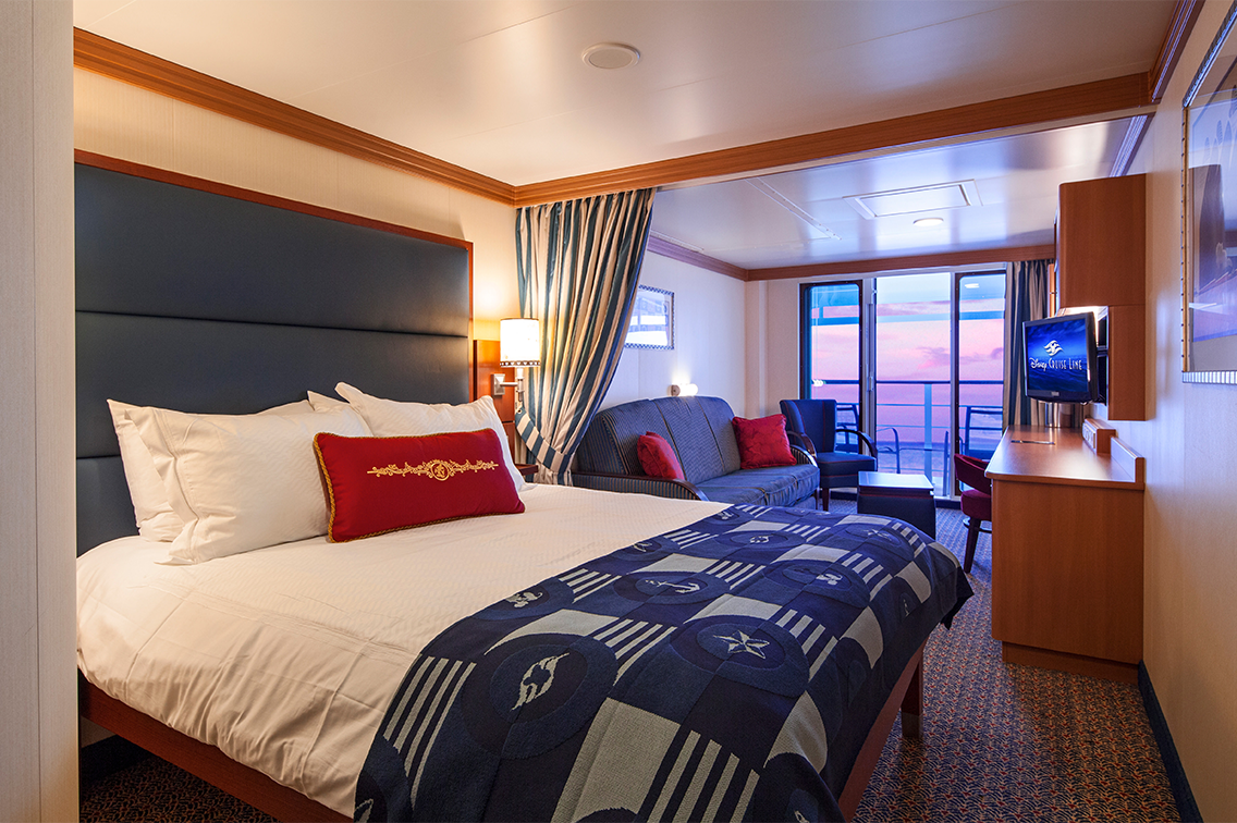 Une cabine avec un très grand lit, un canapé, des chaises, un balcon, une vue d'un coucher de soleil