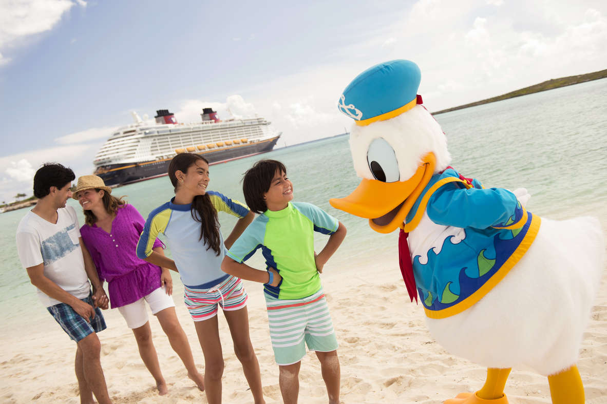 Une famille parle à Donald Duck sur une plage près d'un navire de croisière