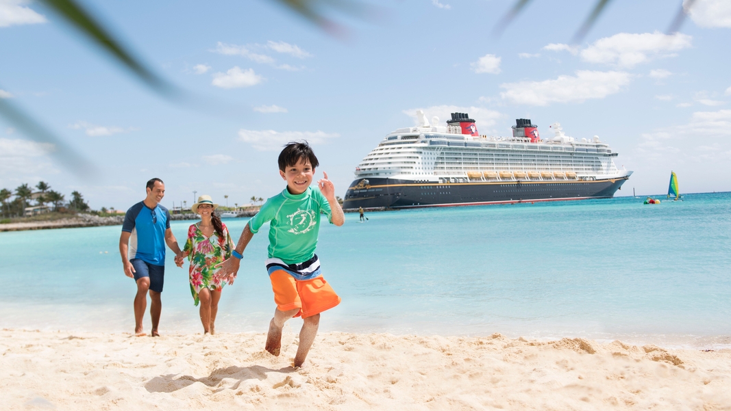Un homme et une femme suivent un garçon qui court sur une plage près d'un navire de croisière