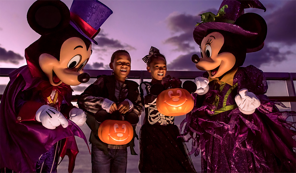 Deux enfants tiennent des seaux de bonbons à côté de Minnie et Mickey Mouse en costume d'Halloween