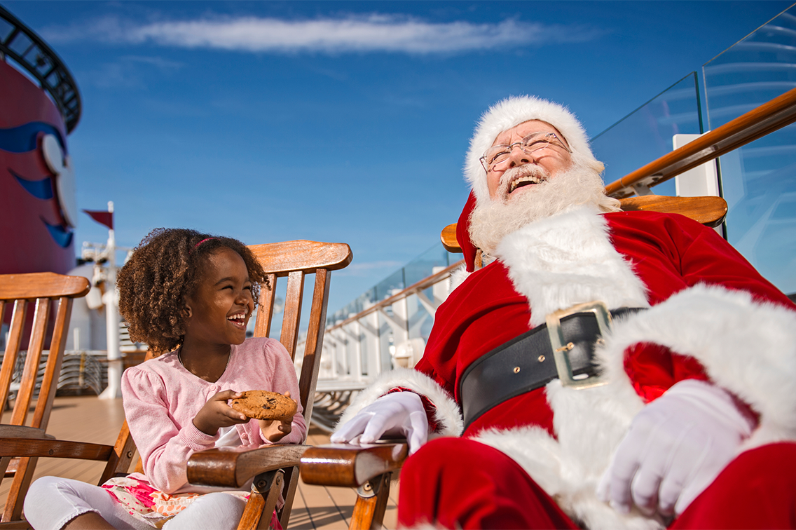Une fillette offre un biscuit au père Noël, assis sur des chaises en bois sur une croisière Disney