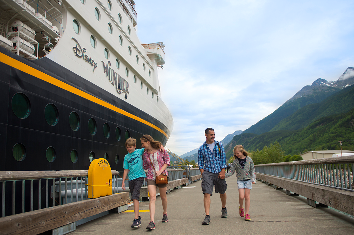 Une famille marche à côté d'un navire de croisière et près des montagnes