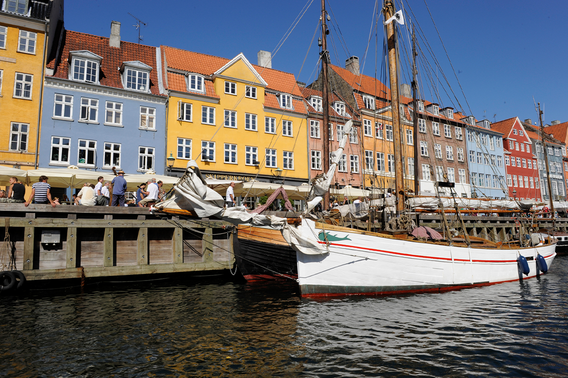 Des bâtiments colorés et des embarcations bordent un port de Copenhague, et se reflètent dans l'eau